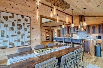 kitchen featuring wall chimney exhaust hood, light wood-type flooring, vaulted ceiling, decorative light fixtures, and wooden walls