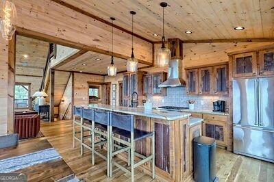 kitchen with lofted ceiling, stainless steel fridge, a kitchen island with sink, ventilation hood, and light hardwood / wood-style floors