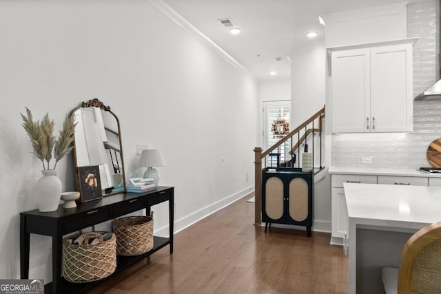 interior space with wall chimney range hood, crown molding, decorative backsplash, dark hardwood / wood-style floors, and white cabinetry