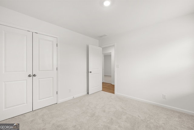 unfurnished bedroom with light colored carpet and a closet