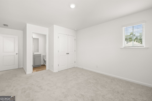 unfurnished bedroom with a closet, light colored carpet, and connected bathroom