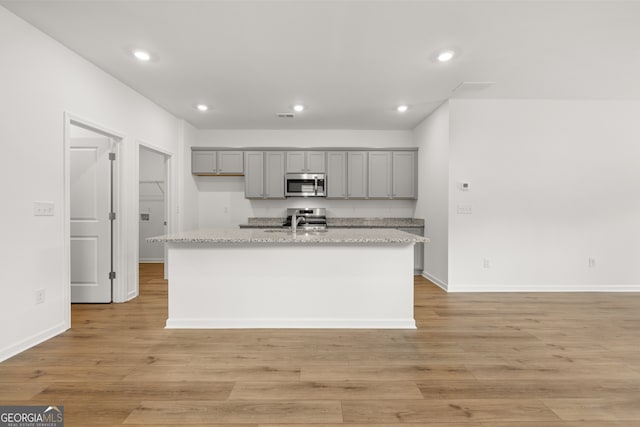 kitchen featuring light hardwood / wood-style floors, a kitchen island with sink, light stone counters, and gray cabinetry