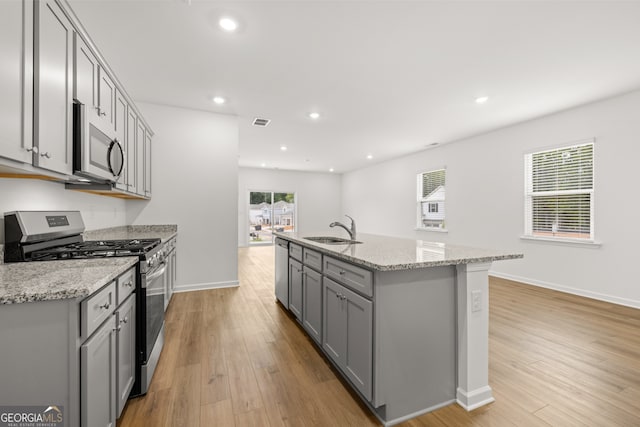 kitchen with a wealth of natural light, a kitchen island with sink, sink, and stainless steel appliances