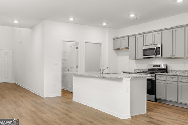 kitchen with a center island with sink, light wood-type flooring, light stone counters, and stainless steel appliances