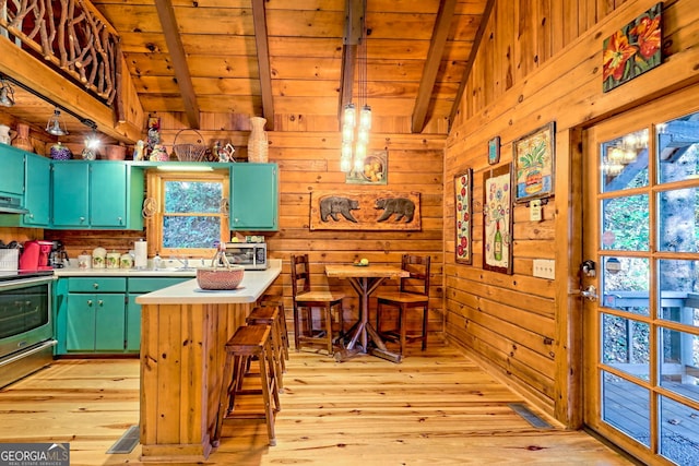 kitchen featuring stainless steel stove, wood walls, lofted ceiling with beams, and light hardwood / wood-style floors