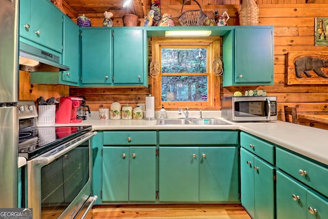 kitchen with wood walls, sink, appliances with stainless steel finishes, green cabinets, and light hardwood / wood-style floors