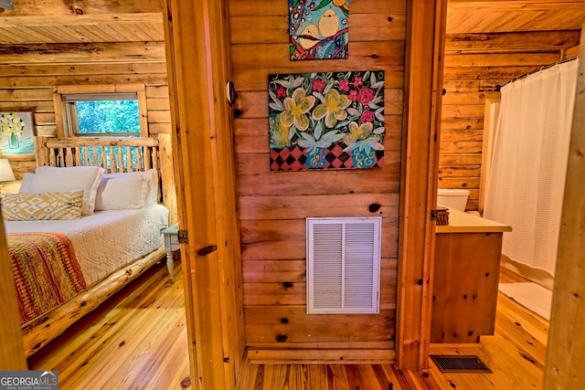 bedroom with log walls, beamed ceiling, wood ceiling, and light hardwood / wood-style floors