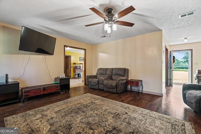 living room featuring dark wood-type flooring, ceiling fan, and a textured ceiling