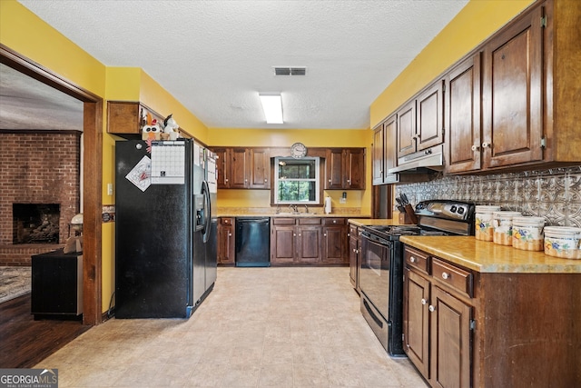 kitchen with sink, a brick fireplace, a textured ceiling, black appliances, and decorative backsplash