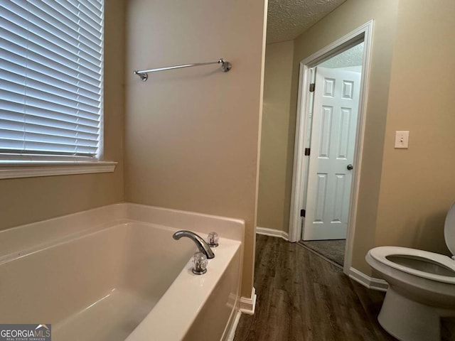 bathroom with wood-type flooring, a textured ceiling, a bathtub, and toilet