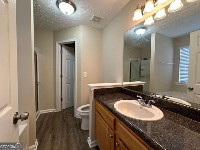 bathroom with vanity, hardwood / wood-style flooring, a shower with door, toilet, and a textured ceiling