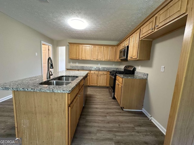 kitchen with an island with sink, sink, a textured ceiling, appliances with stainless steel finishes, and dark hardwood / wood-style floors