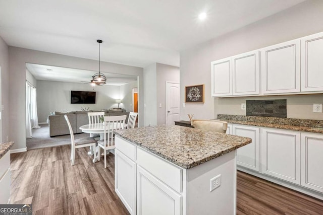 kitchen with light stone counters, a kitchen island, hardwood / wood-style flooring, and white cabinetry