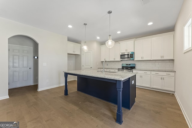 kitchen featuring white cabinetry, a kitchen island with sink, light stone countertops, appliances with stainless steel finishes, and pendant lighting