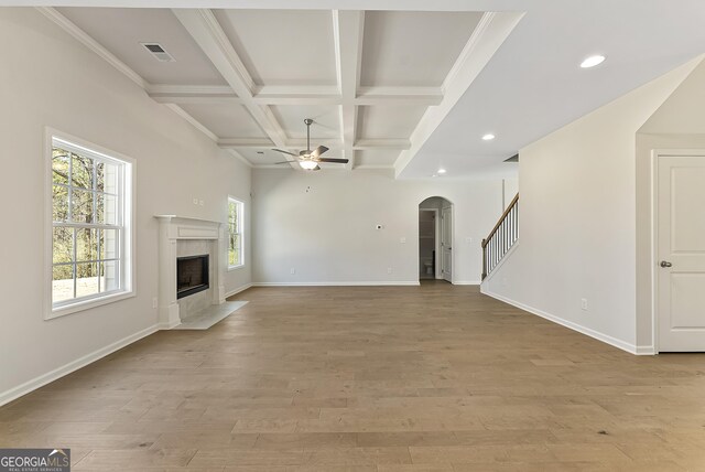 unfurnished living room featuring coffered ceiling, light hardwood / wood-style flooring, a high end fireplace, beamed ceiling, and ceiling fan