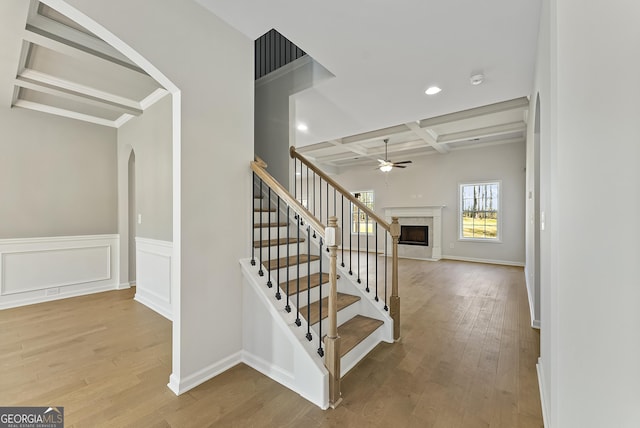 stairway featuring coffered ceiling, hardwood / wood-style flooring, a high end fireplace, and beam ceiling