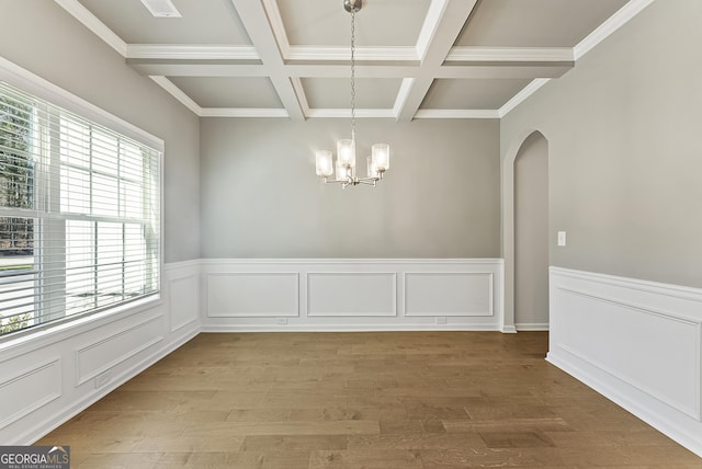 unfurnished dining area with coffered ceiling, a chandelier, wood-type flooring, and beamed ceiling