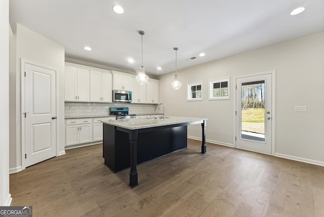 kitchen with appliances with stainless steel finishes, sink, white cabinets, hanging light fixtures, and a kitchen island with sink