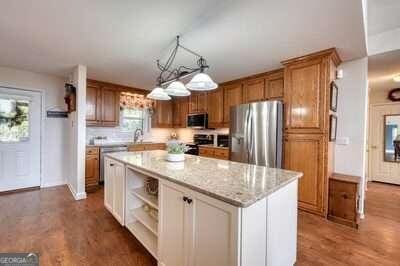 kitchen with wood-type flooring, decorative light fixtures, light stone countertops, appliances with stainless steel finishes, and a center island