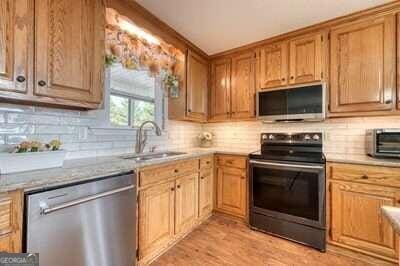 kitchen featuring sink, tasteful backsplash, appliances with stainless steel finishes, light stone countertops, and light hardwood / wood-style floors