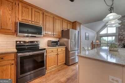 kitchen with vaulted ceiling, appliances with stainless steel finishes, hanging light fixtures, and light hardwood / wood-style floors