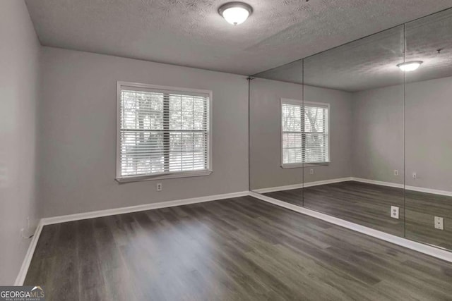 unfurnished room with a textured ceiling, a wealth of natural light, and dark hardwood / wood-style flooring