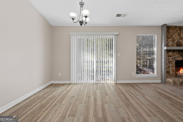 unfurnished living room with a notable chandelier, light wood-type flooring, a fireplace, and a textured ceiling