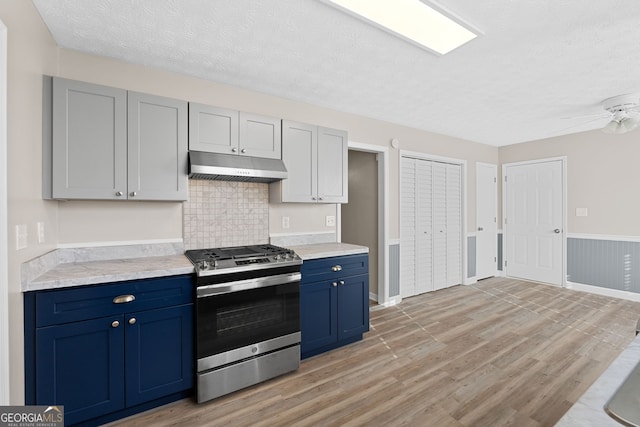 kitchen with stainless steel gas range oven, a textured ceiling, blue cabinetry, light wood-style flooring, and under cabinet range hood