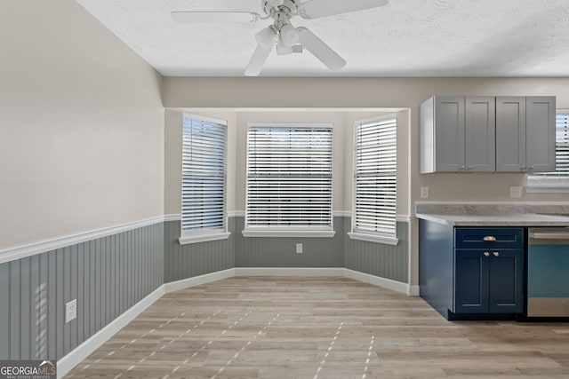 kitchen with ceiling fan, wainscoting, light wood-style floors, a textured ceiling, and stainless steel dishwasher