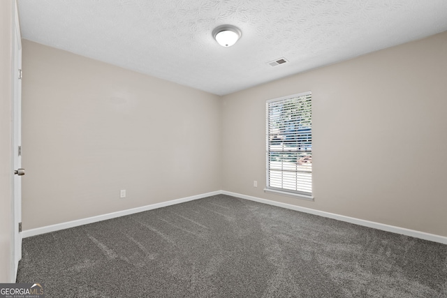 empty room with dark carpet, a textured ceiling, baseboards, and visible vents