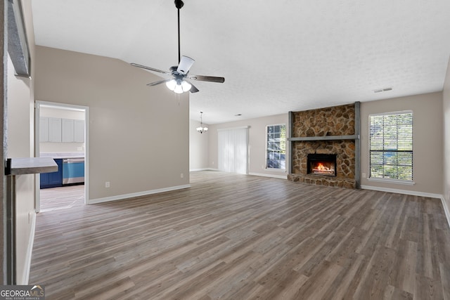 unfurnished living room featuring ceiling fan with notable chandelier, a stone fireplace, dark hardwood / wood-style floors, and a textured ceiling