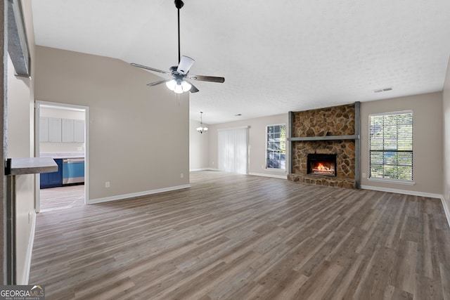 unfurnished living room with a fireplace, ceiling fan with notable chandelier, baseboards, wood finished floors, and visible vents