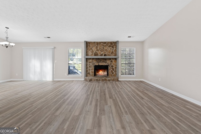 unfurnished living room with wood-type flooring, a textured ceiling, a fireplace, and an inviting chandelier