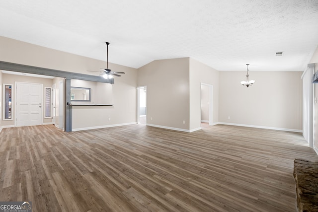 unfurnished living room featuring ceiling fan with notable chandelier, baseboards, wood finished floors, vaulted ceiling, and visible vents