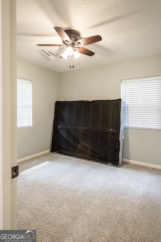 carpeted empty room with ceiling fan, a textured ceiling, and a healthy amount of sunlight