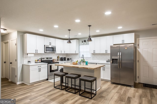 kitchen featuring white cabinets, a center island with sink, stainless steel appliances, and hanging light fixtures