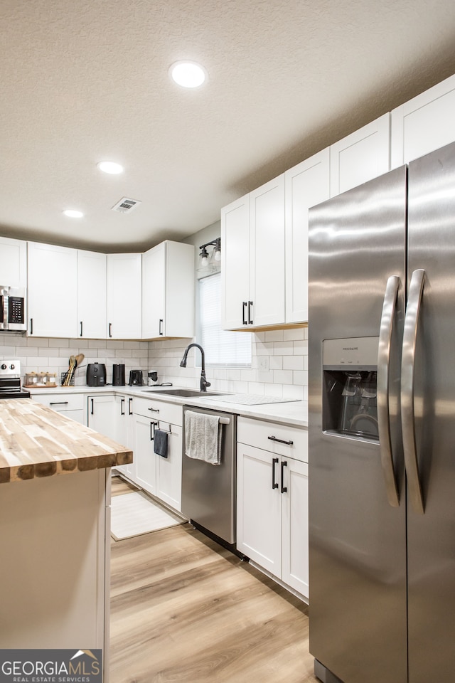 kitchen with light wood-type flooring, stainless steel appliances, white cabinets, butcher block counters, and sink