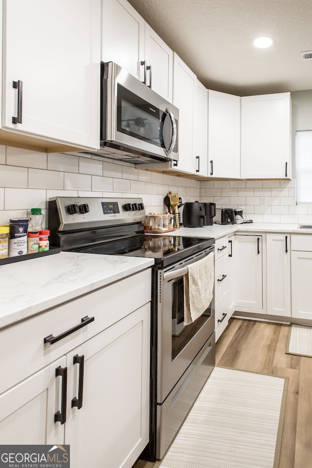 kitchen featuring light wood-type flooring, stainless steel appliances, light stone countertops, backsplash, and white cabinetry