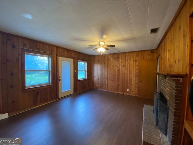 unfurnished living room featuring ceiling fan, a fireplace, wood walls, and dark wood-type flooring