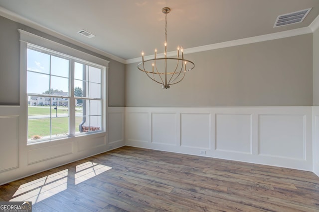 unfurnished dining area with wood-type flooring, an inviting chandelier, and ornamental molding