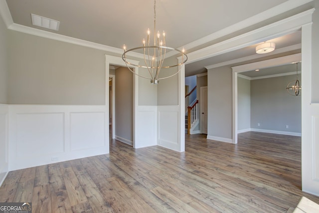 unfurnished dining area with hardwood / wood-style flooring, ornamental molding, and a notable chandelier