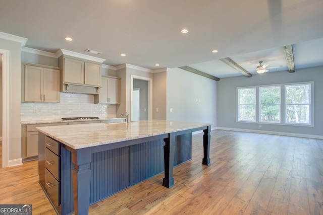 kitchen featuring backsplash, light wood-type flooring, a large island, beam ceiling, and light stone counters