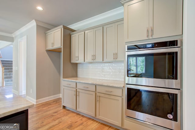 kitchen featuring light wood-type flooring, stainless steel double oven, light stone countertops, and crown molding