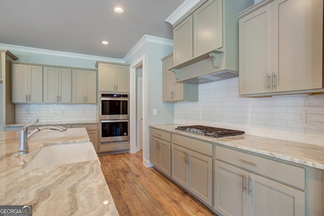 kitchen with light wood-type flooring, backsplash, stainless steel appliances, crown molding, and sink