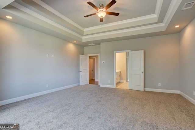 unfurnished bedroom with light carpet, a tray ceiling, ceiling fan, and ensuite bathroom