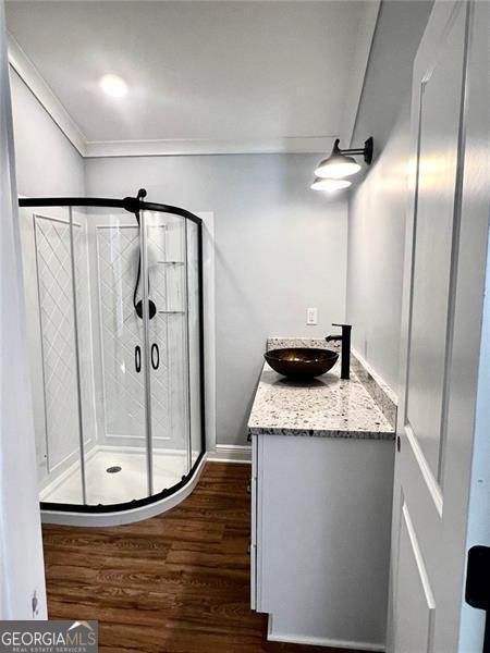 bathroom with wood-type flooring, crown molding, a shower with door, and vanity