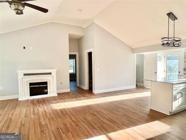 unfurnished living room featuring ceiling fan with notable chandelier, light hardwood / wood-style floors, crown molding, and vaulted ceiling