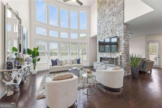 living room with ceiling fan, a stone fireplace, plenty of natural light, and dark wood-type flooring