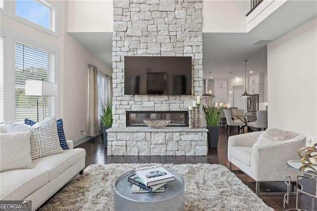 living room featuring a stone fireplace, a towering ceiling, and dark wood-type flooring