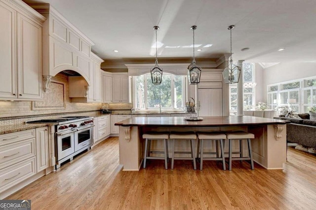 kitchen featuring light wood-type flooring, hanging light fixtures, white cabinetry, range with two ovens, and dark stone counters